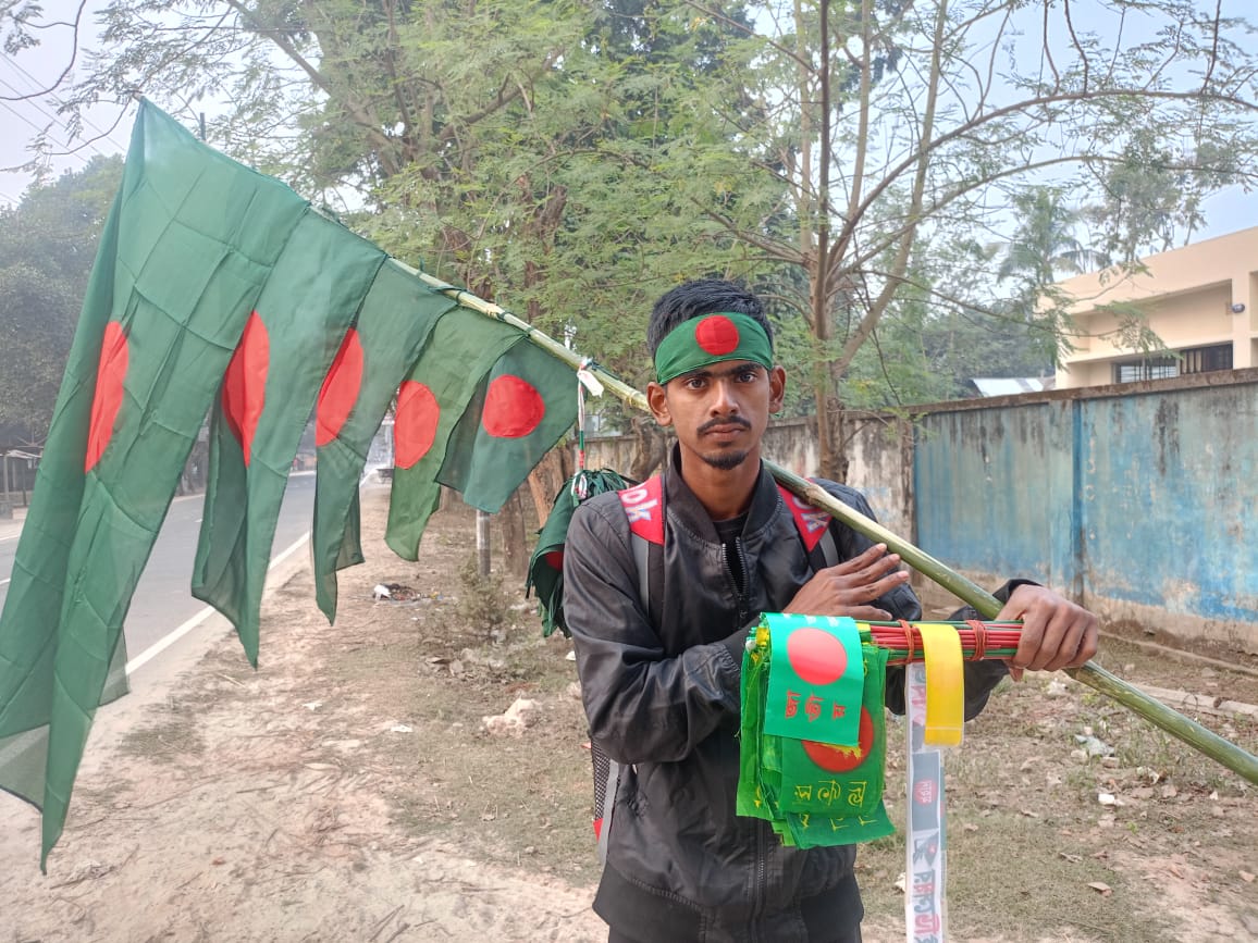 পীরগঞ্জে  বিজয়ের মাসে লাল-সবুজের ফেরিওয়ালা জাতীয় পতাকা কাঁধে ফেরিওয়ালা মো টুটুল 
